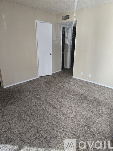 A carpeted room with a door and a wall socket.