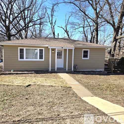 A small house with a white door and windows is surrounded by trees.