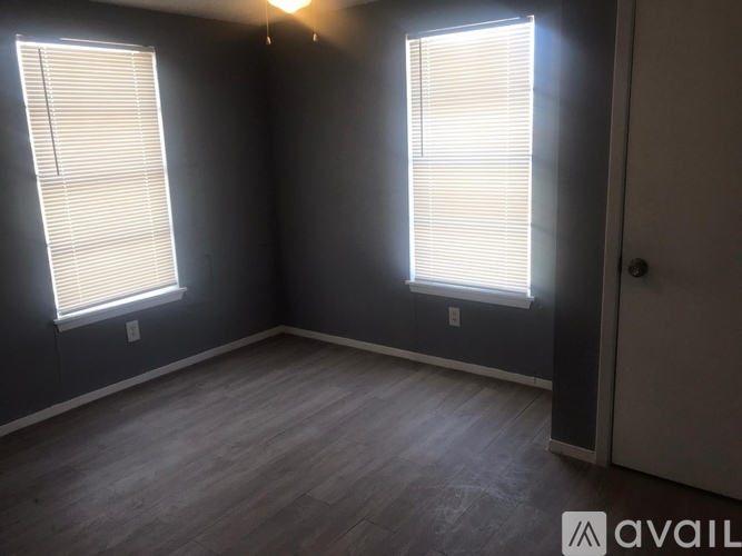 A room with a wooden floor and two windows with blinds.