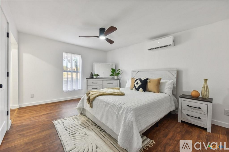 A bedroom with a large bed, a ceiling fan, and a nightstand with a vase on it.