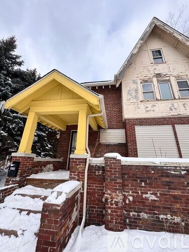 A house with a yellow front porch and snow on the ground.