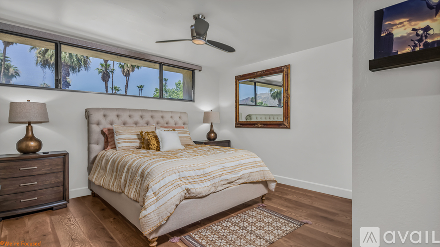 A bedroom with a large bed, a ceiling fan, and a flat-screen TV mounted on the wall.