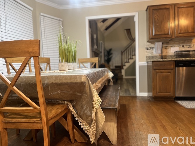 A dining table with a wooden chair and a tablecloth is in the foreground of a kitchen.