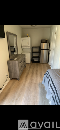 A small room with a bed, a dresser, a mirror, a fridge, and a small white cabinet.