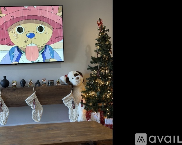 A dog is sitting in front of a Christmas tree with stockings hanging on a shelf.