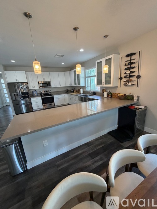 A modern kitchen with a long island and white chairs.