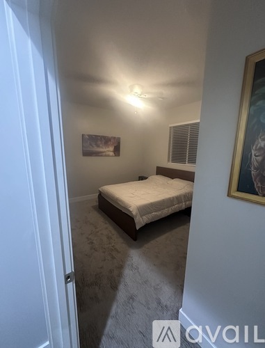 A bedroom with a bed, a painting on the wall, and a window with blinds.
