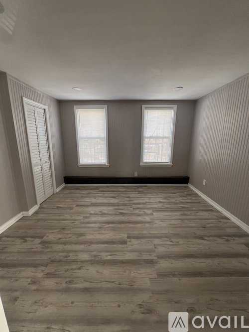 A room with wooden flooring and a kitchen area in the background.
