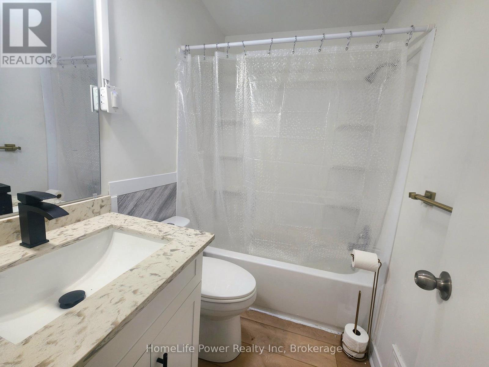 A white bathroom with a marble counter top and a glass shower enclosure.