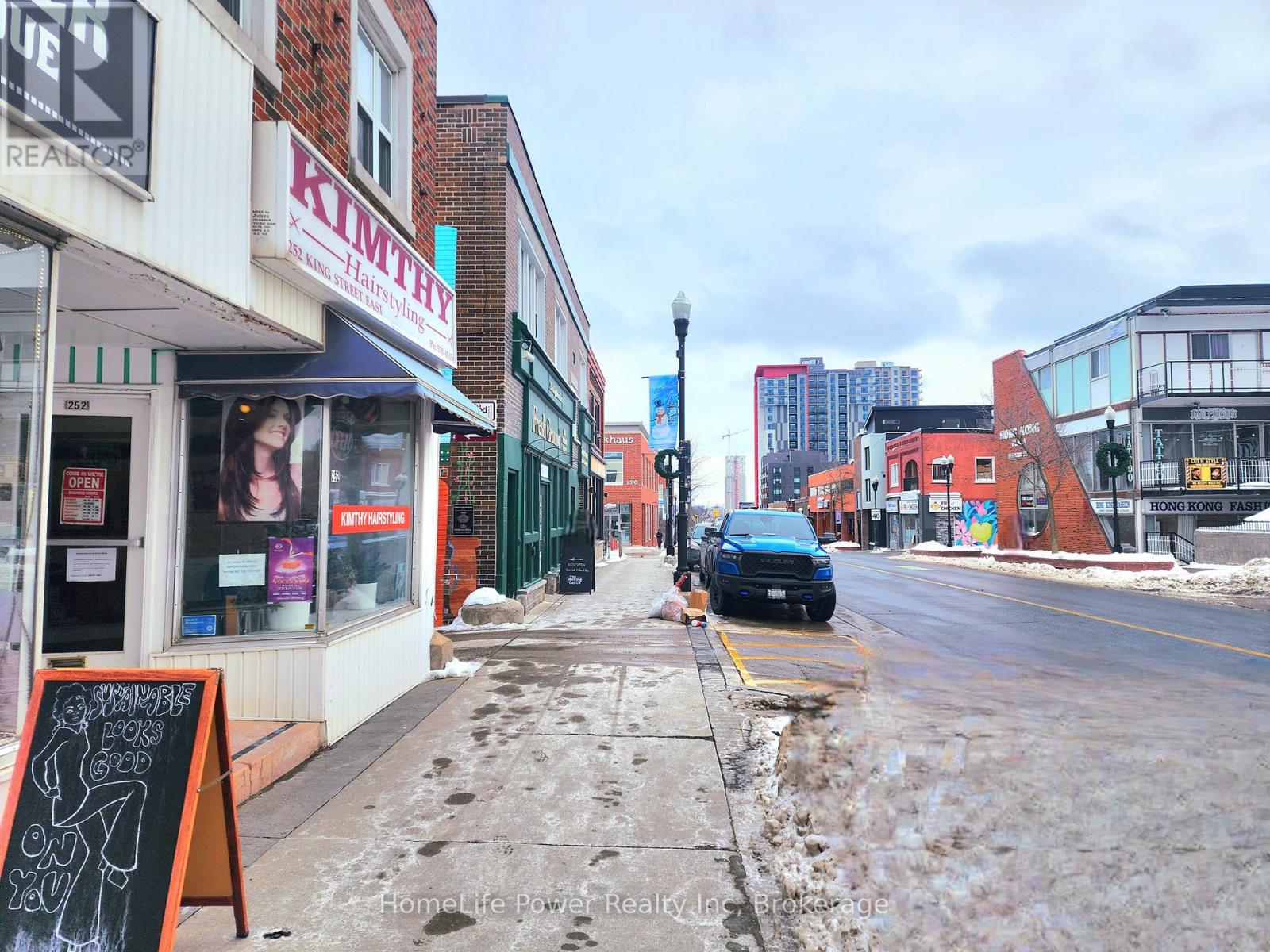 A street view of a city with buildings, a car, and a sign that says "KIMTTY".