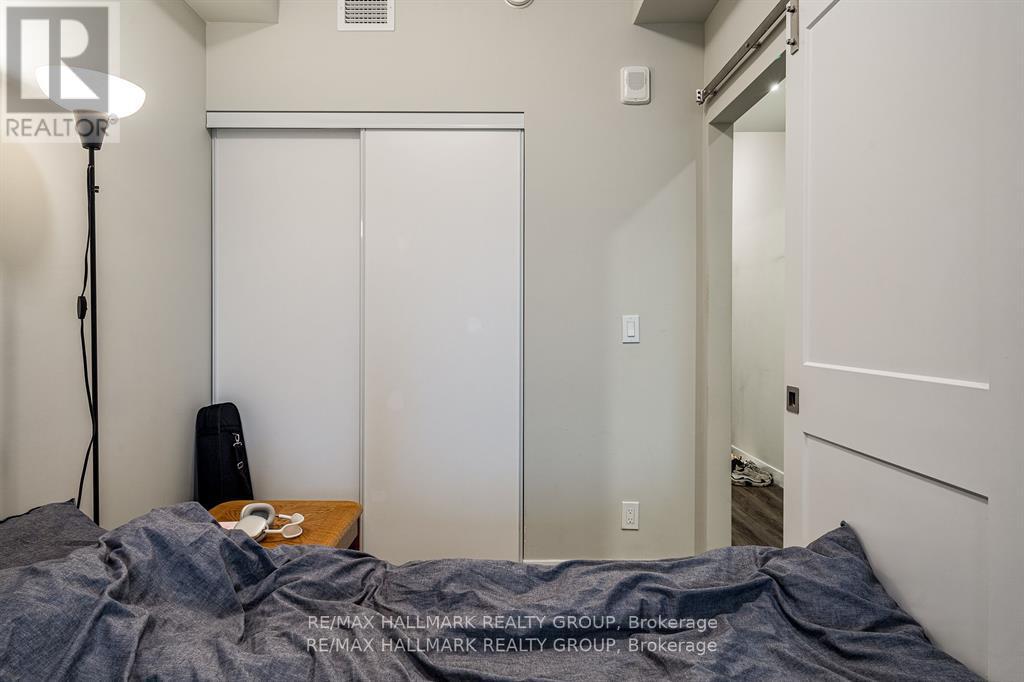 A bedroom with a bed covered in a grey blanket, a lamp on the left, and a white closet with a mirror.