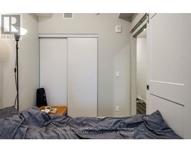 A bedroom with a bed covered in a grey blanket, a lamp on the left, and a white closet with a mirror.