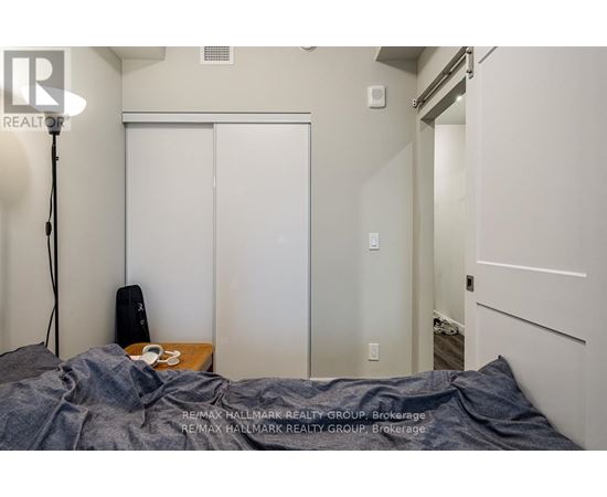 A bedroom with a bed covered in a grey blanket, a lamp on the left, and a white closet with a mirror.