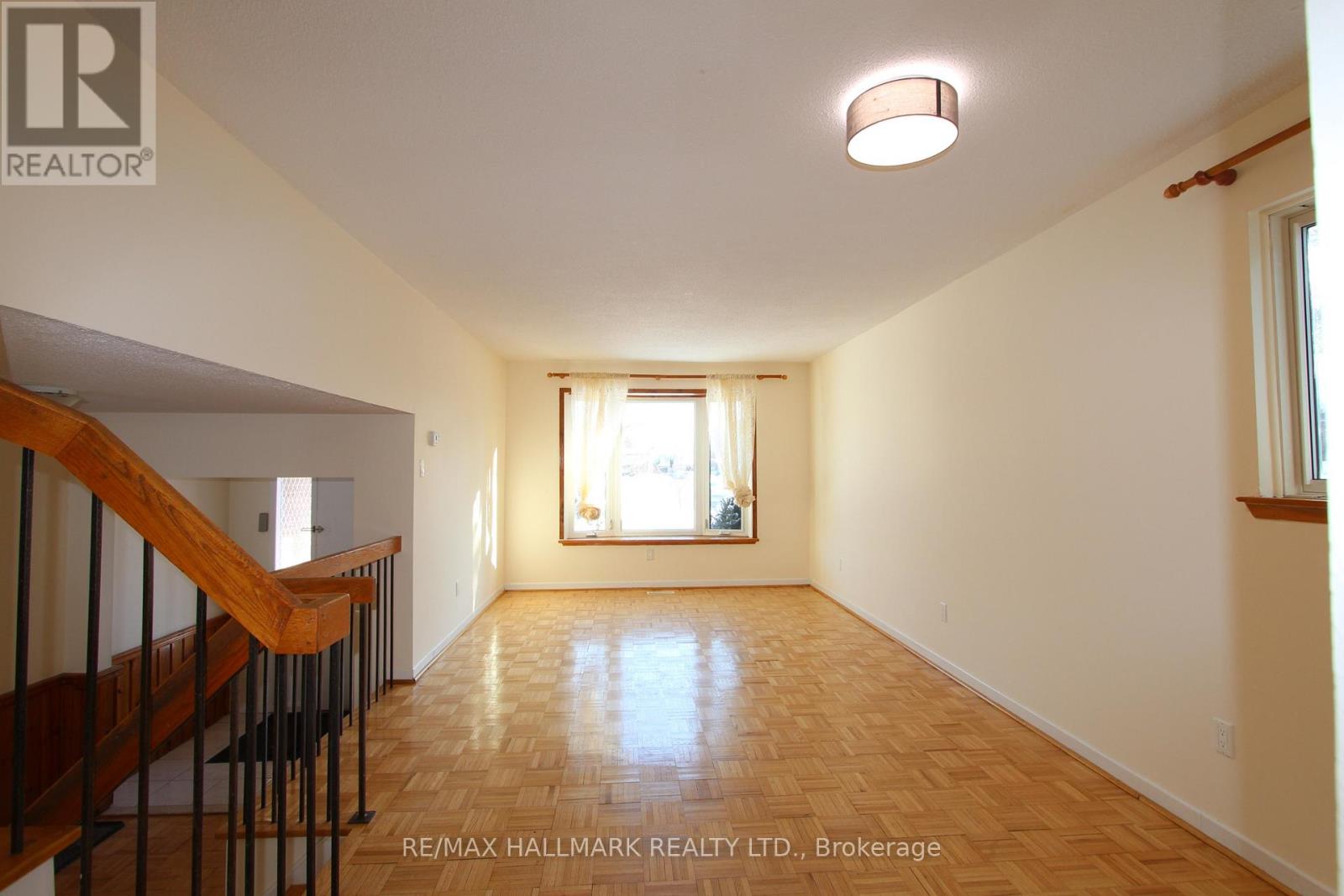 A spacious room with wooden flooring and a staircase on the left side.