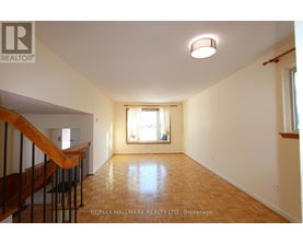 A spacious room with wooden flooring and a staircase on the left side.