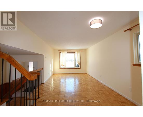 A spacious room with wooden flooring and a staircase on the left side.