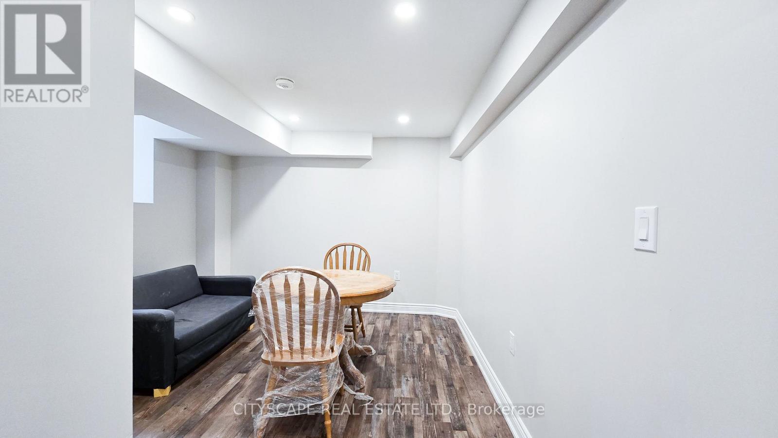 A living room with a black couch, a wooden table, and two chairs.
