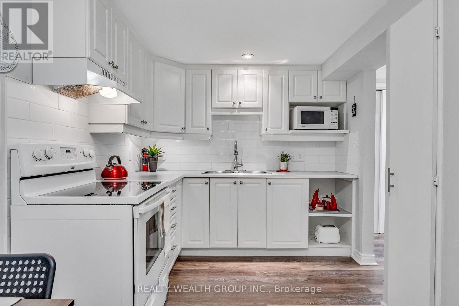 A white kitchen with a red apple on the stove.