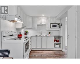 A white kitchen with a red apple on the stove.