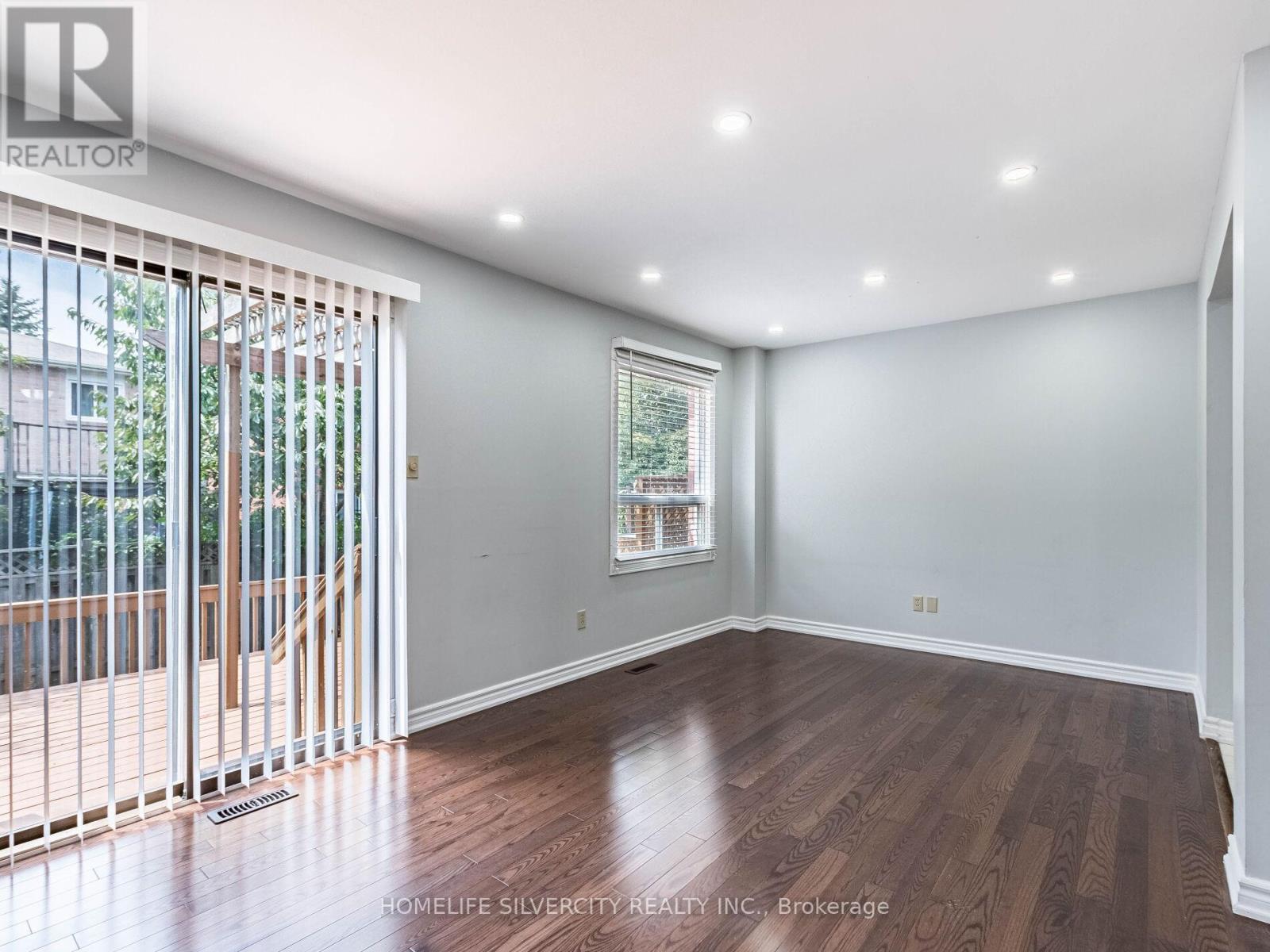 A room with wooden floors and a window with a view of a fence and trees.
