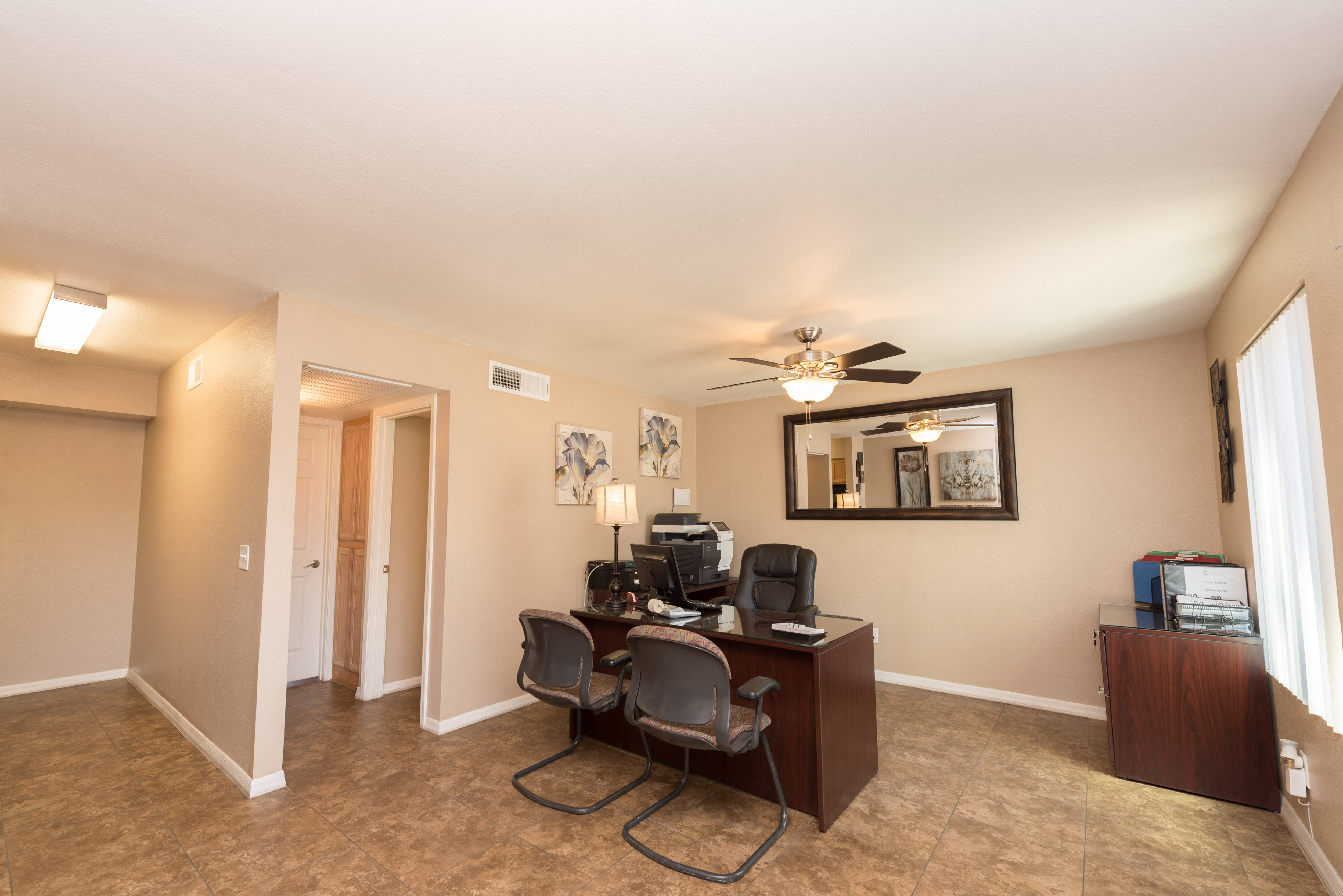 a living room with a desk and chairs and a ceiling fan