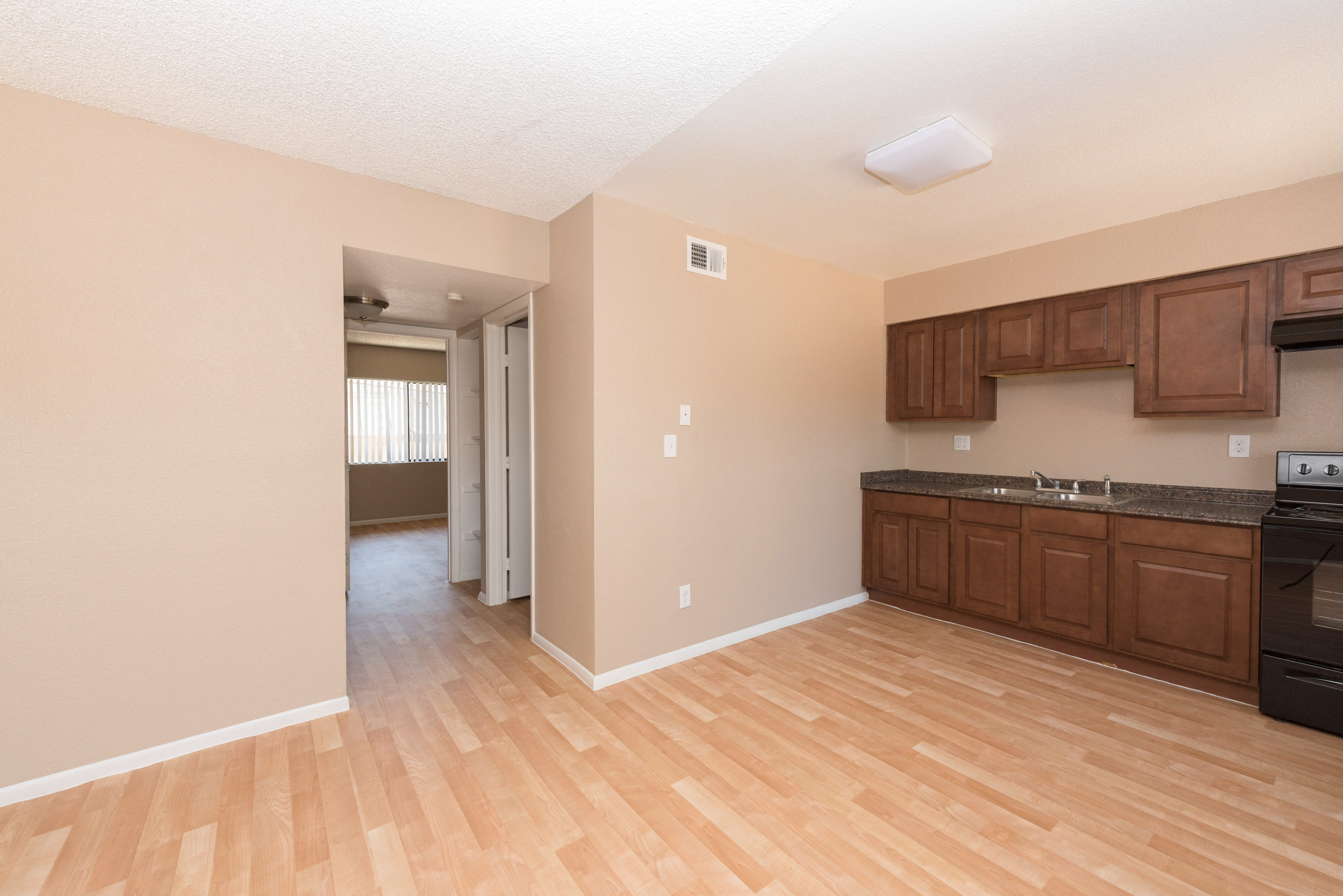 an empty kitchen and living room with wood flooring and wooden cabinets