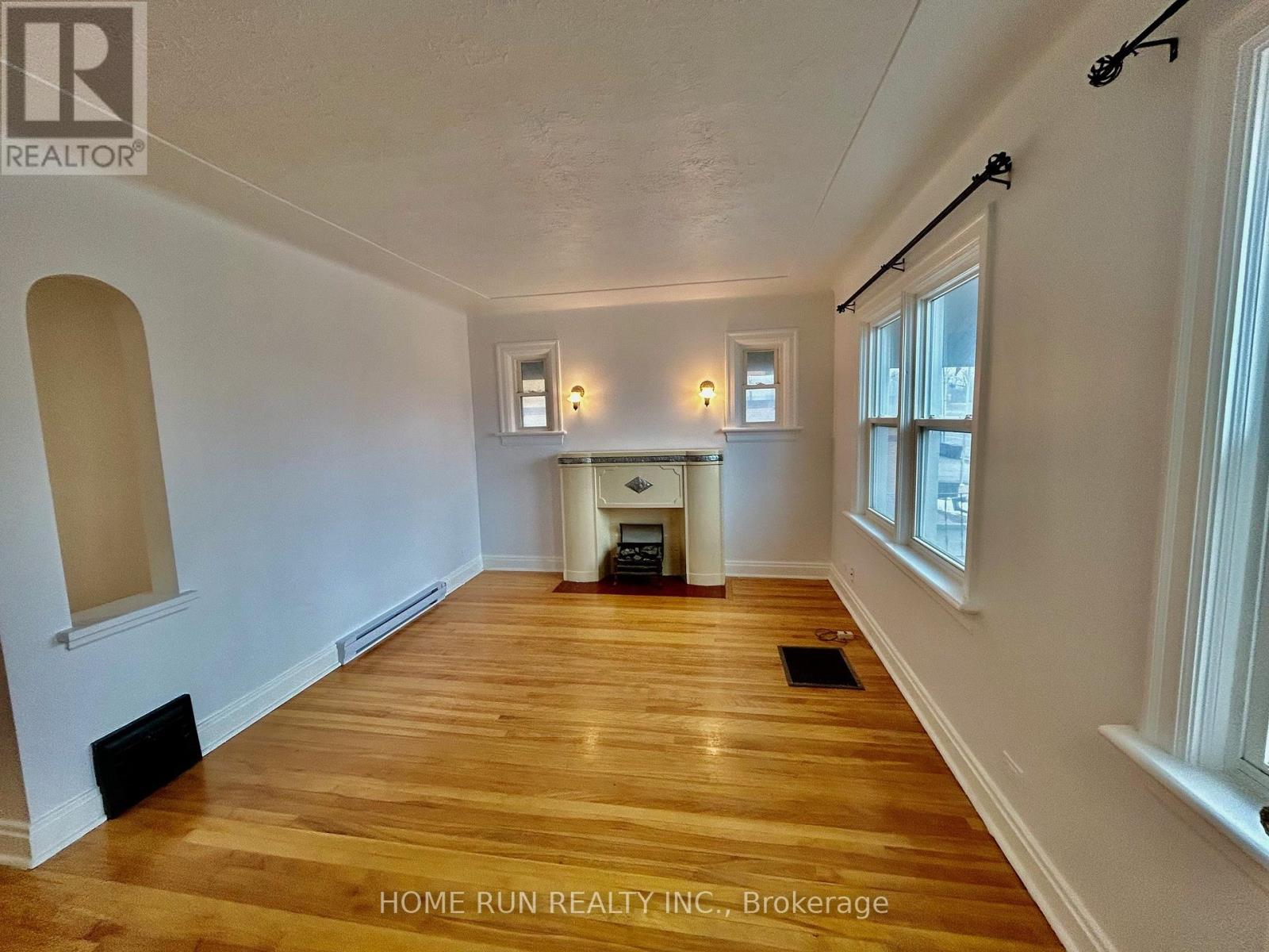 A room with wooden floors and white walls, with a fireplace in the middle.