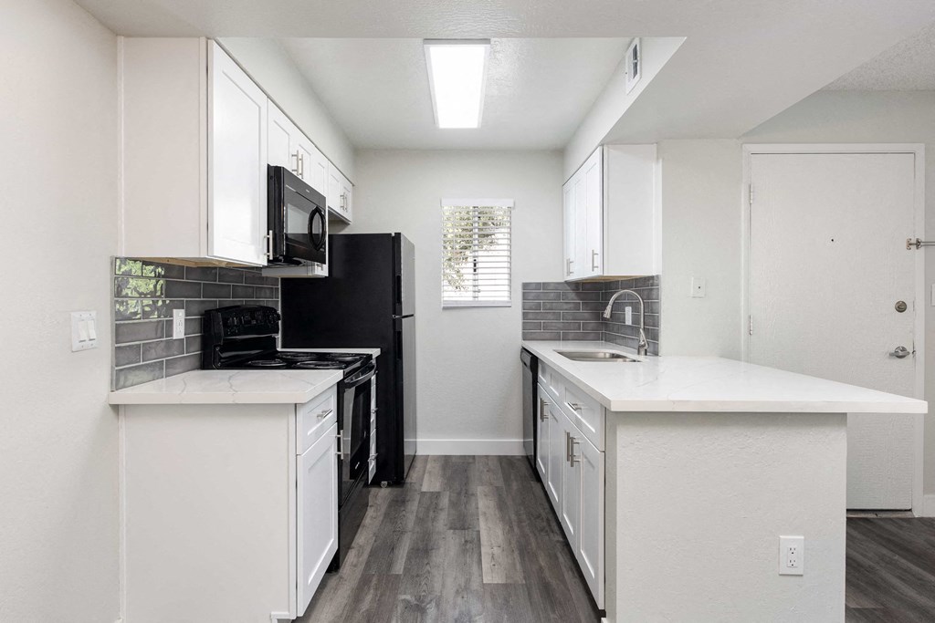 an empty kitchen with white cabinets and a black refrigerator