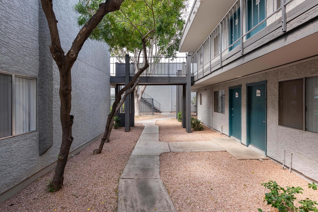 the walkway between the buildings of an apartment complex with trees