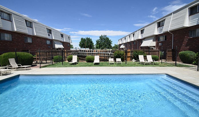 a swimming pool with chairs in front of an apartment building
