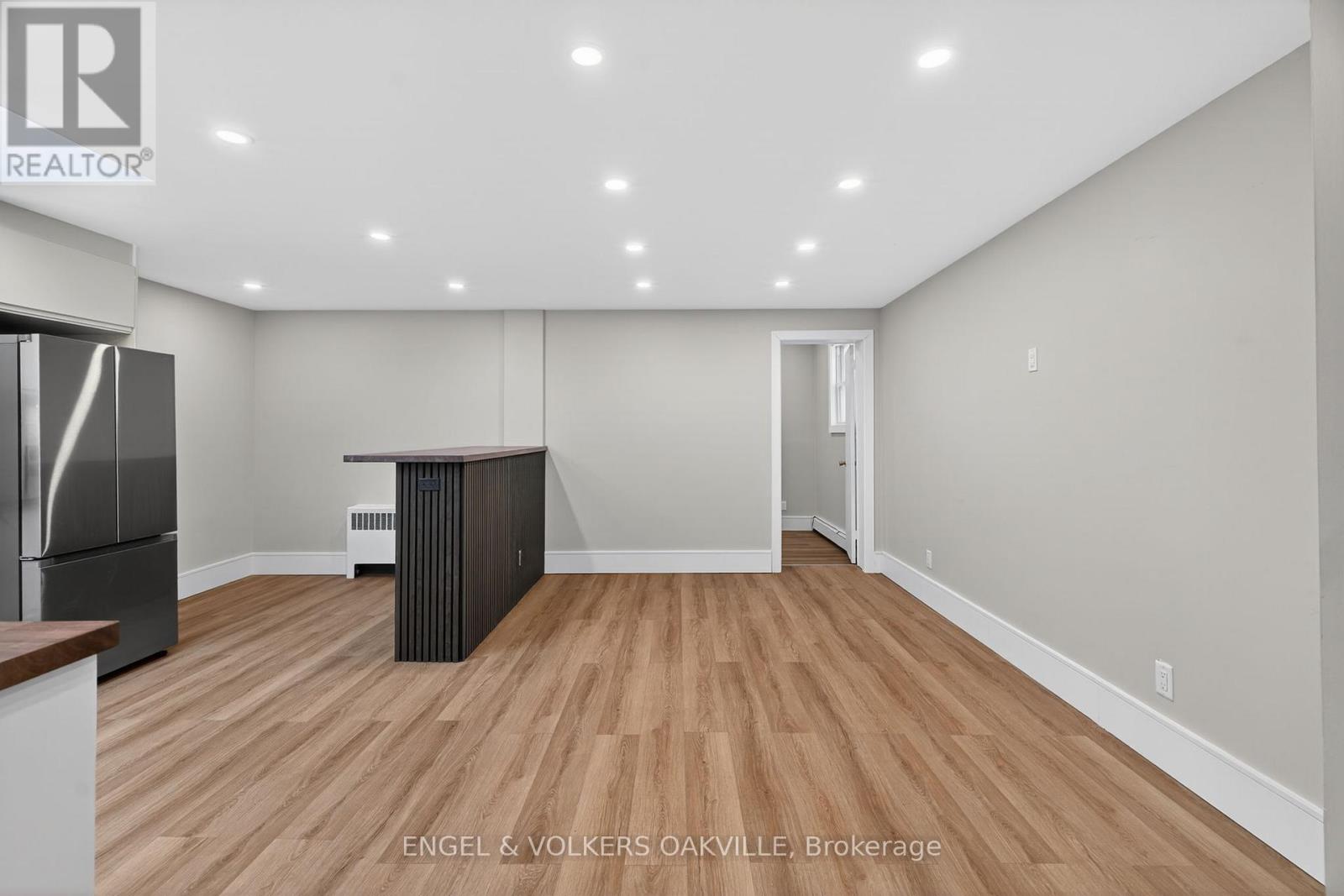 A spacious room with wooden flooring and a refrigerator.