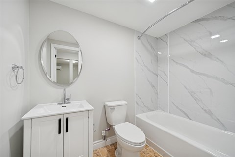 A white bathroom with a marble wall and a round mirror.