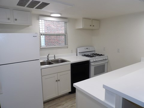 A white kitchen with a fridge, stove, and sink.