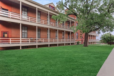 A red building with a balcony and a tree in front.