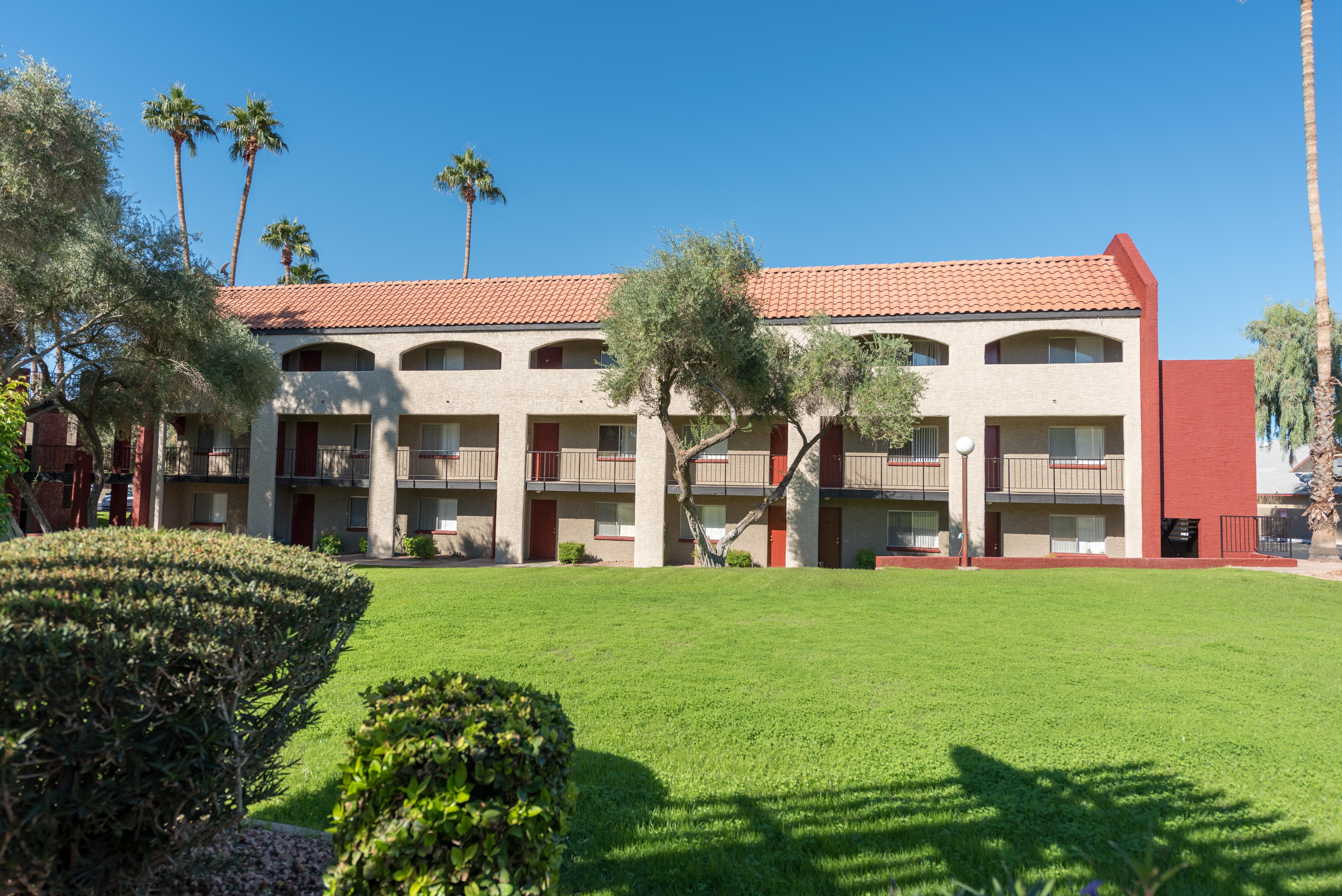 a green lawn in front of a building with palm trees