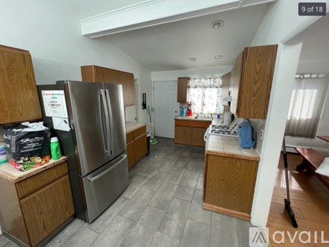 A kitchen with a refrigerator, wooden cabinets, and a tiled floor.