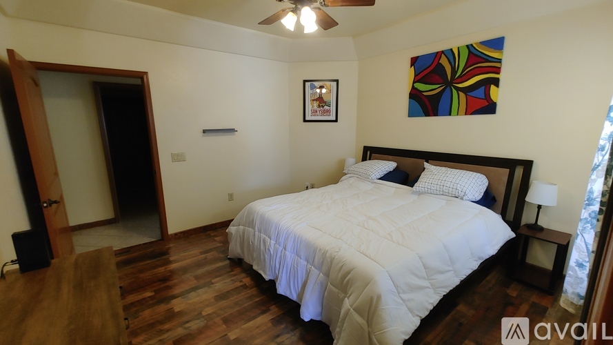 A bedroom with a bed, a ceiling fan, and a painting on the wall.