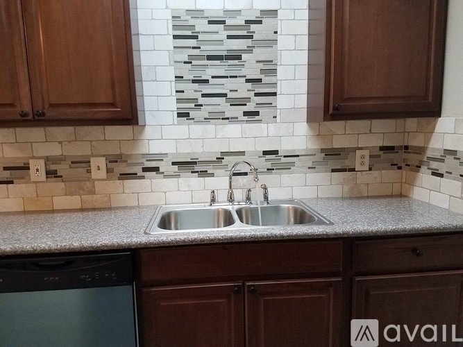 A kitchen with a black dishwasher and brown cabinets.