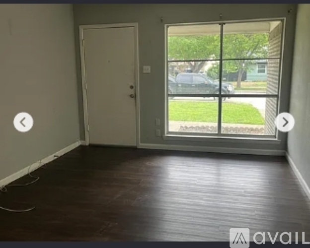 A room with a door and a window showing a view of a car and a fence outside.