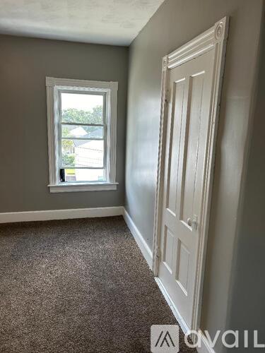 A room with a carpeted floor, a window, and a closed door.
