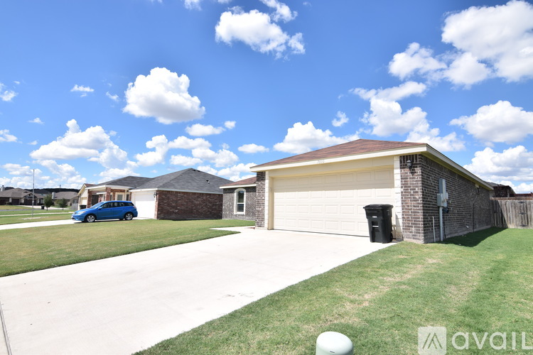A blue car is parked in front of a house with a garage.