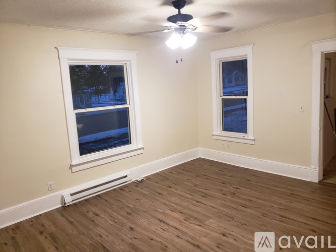 A room with wooden flooring and two windows.