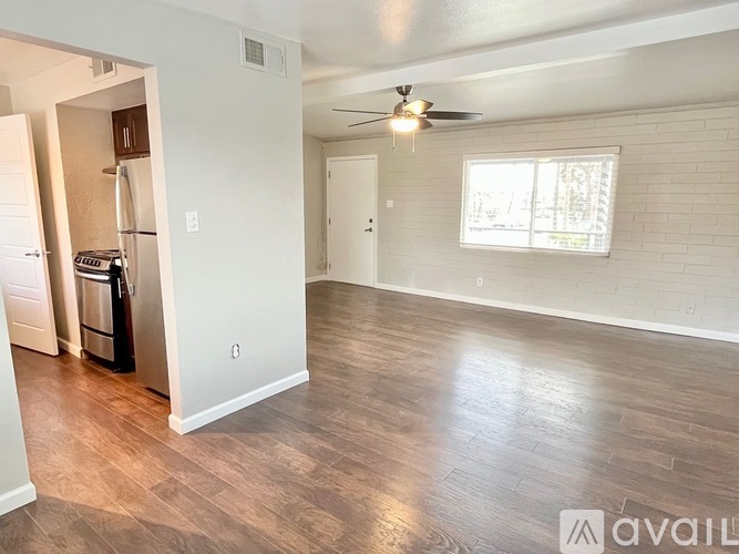 A spacious living room with wood flooring and a window with blinds.