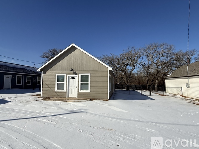 A small house with a white door and a grey roof is surrounded by snow.