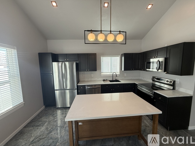 A kitchen with a table in the middle and a fridge to the left.