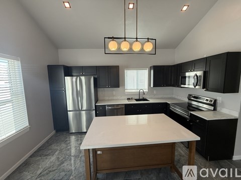 A kitchen with a table in the middle and a fridge to the left.