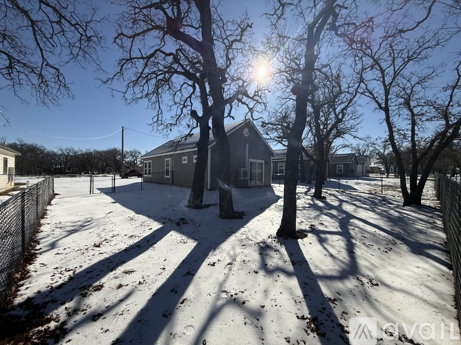 A house with a snow-covered ground and bare trees in front of it.