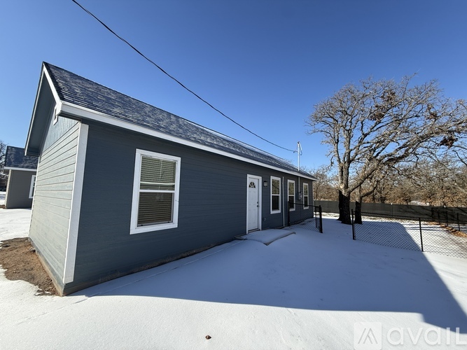 A small house with a grey roof and a white door is surrounded by snow.