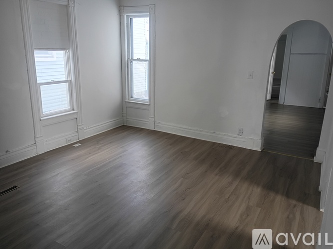 A room with wooden flooring and two windows.