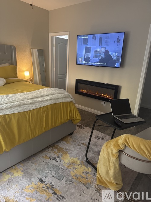 A bedroom with a bed, a TV, a laptop, and a fireplace.